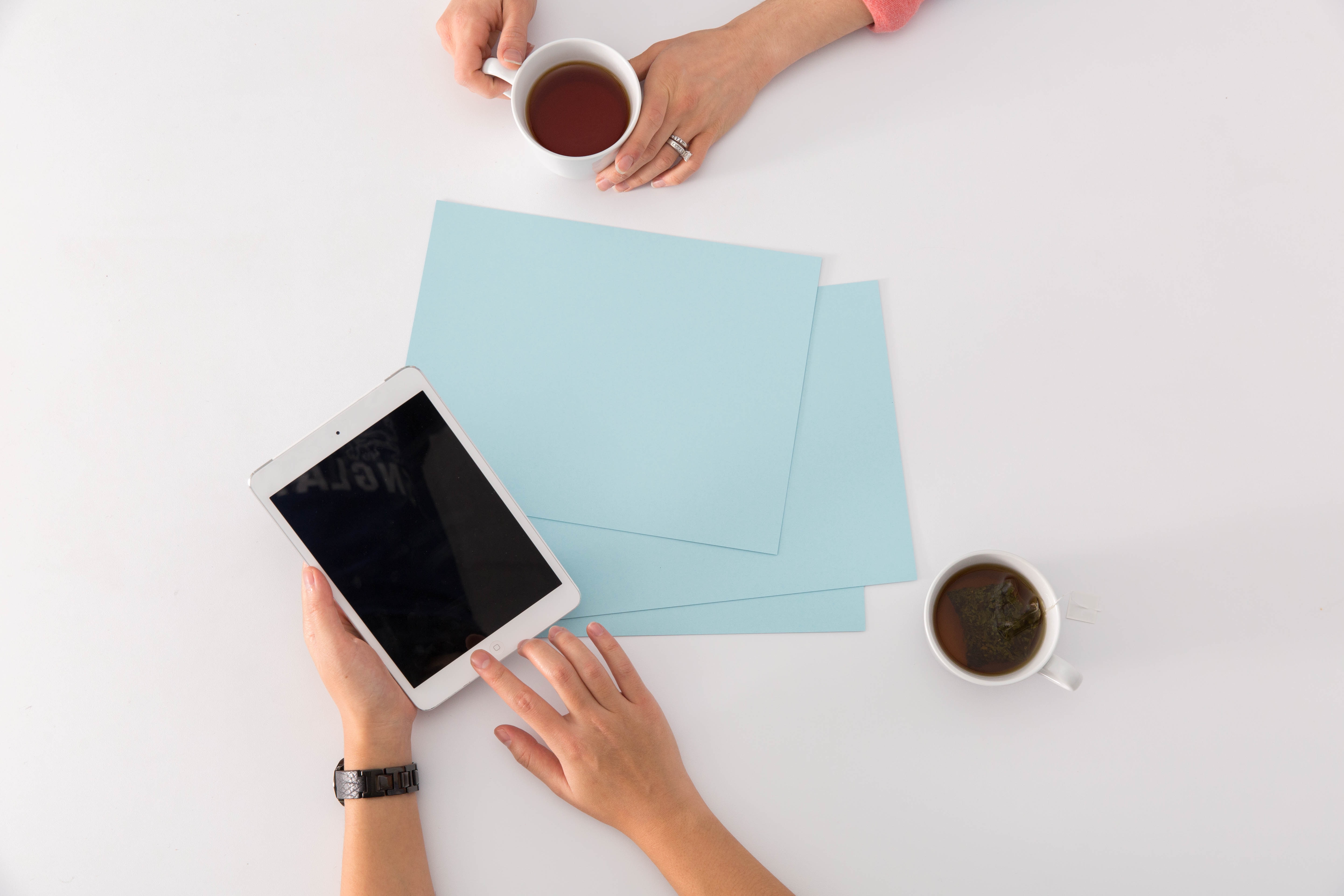 Overhead view of people using a tablet with coffee and documents