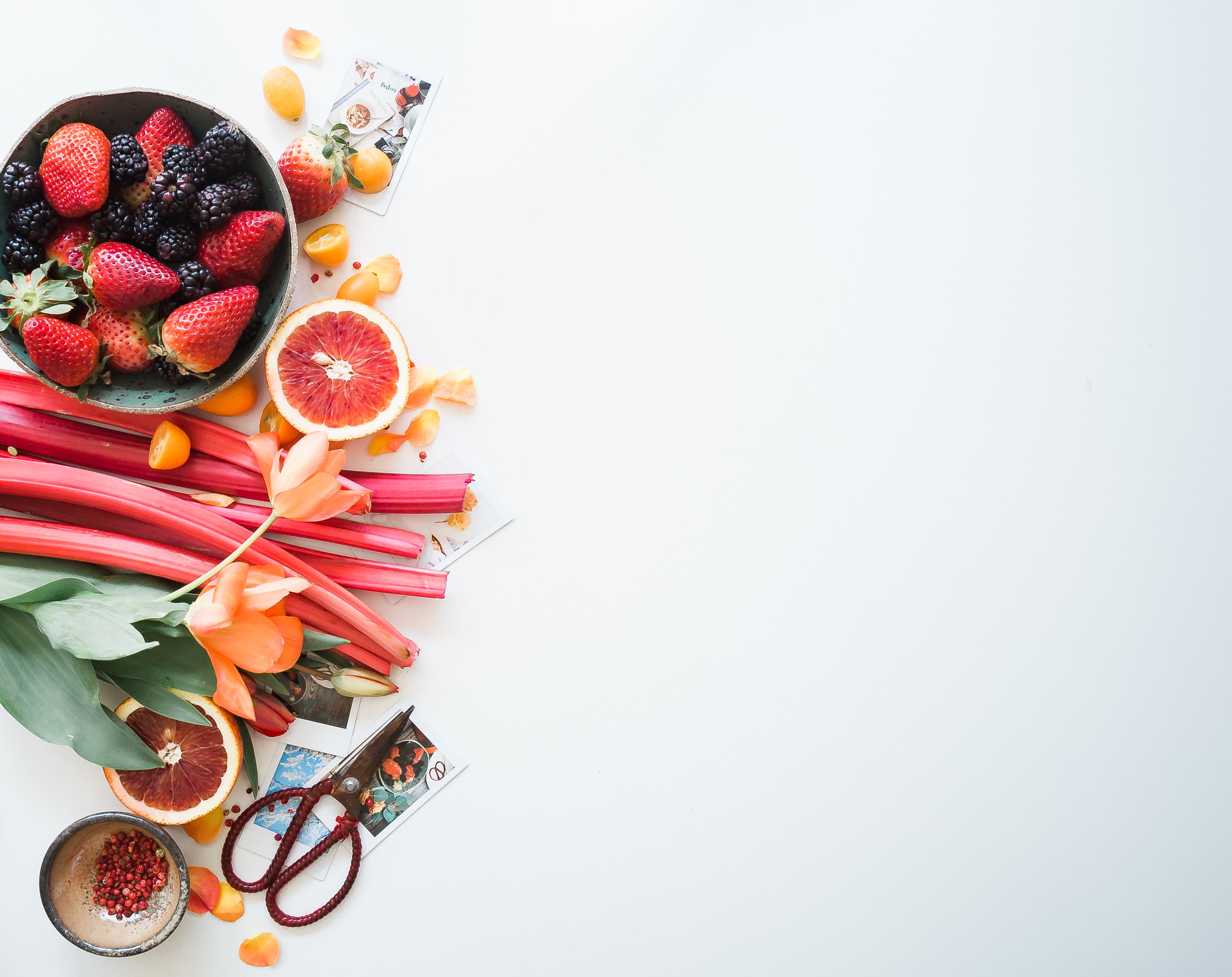 Flat lay arrangement of fresh berries, rhubarb, citrus, and flowers