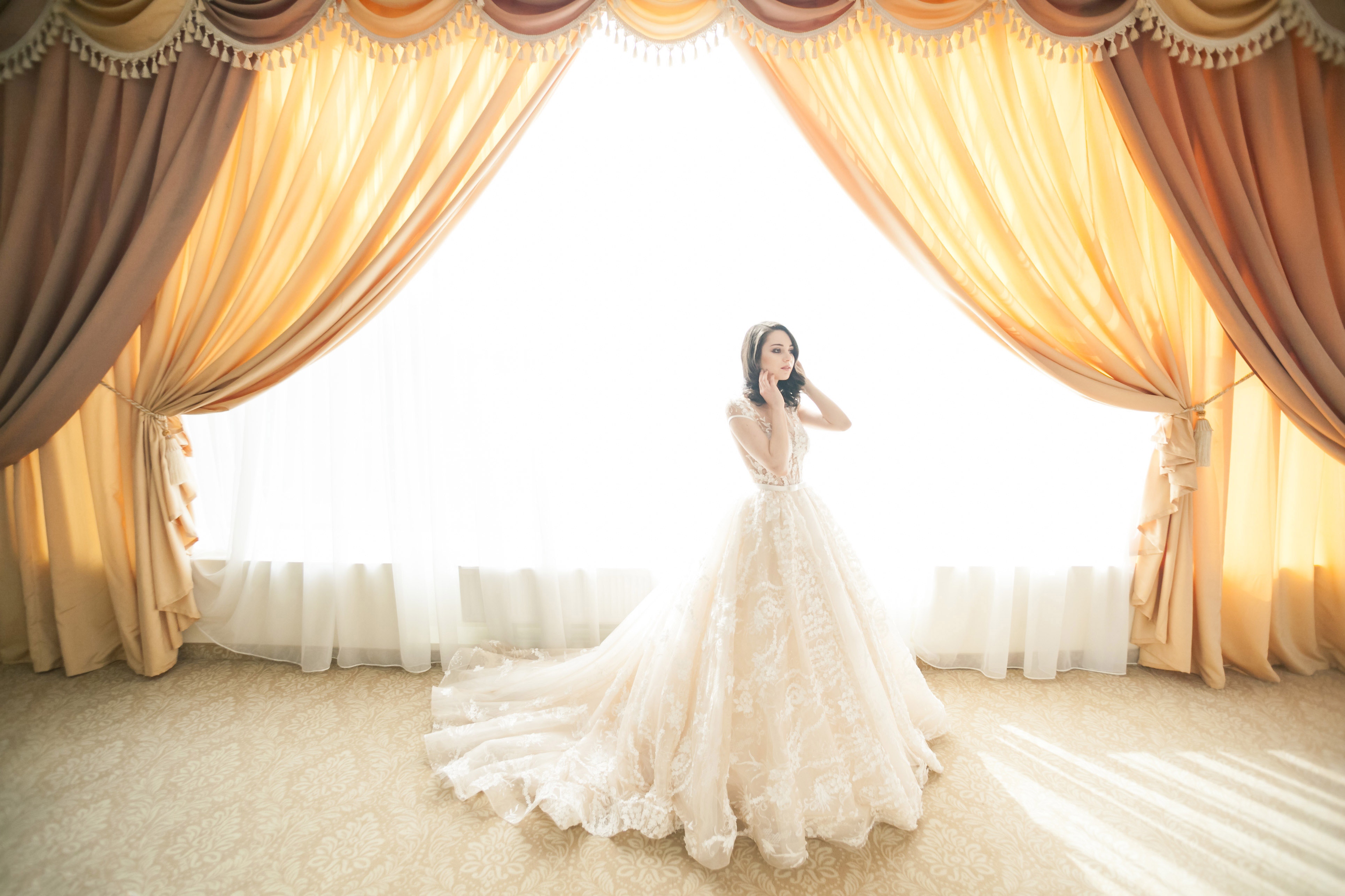 Bride in a white lace wedding dress standing by a window